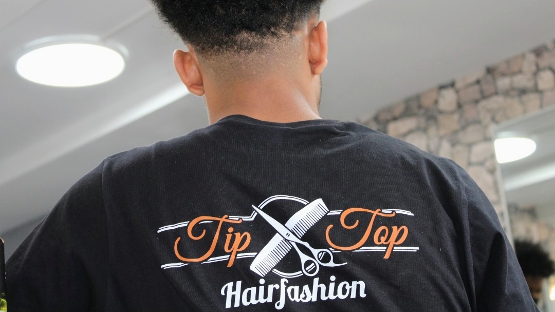 Kapper van TipTop Hairfashion op de rug gezien, met het logo op zijn zwarte shirt